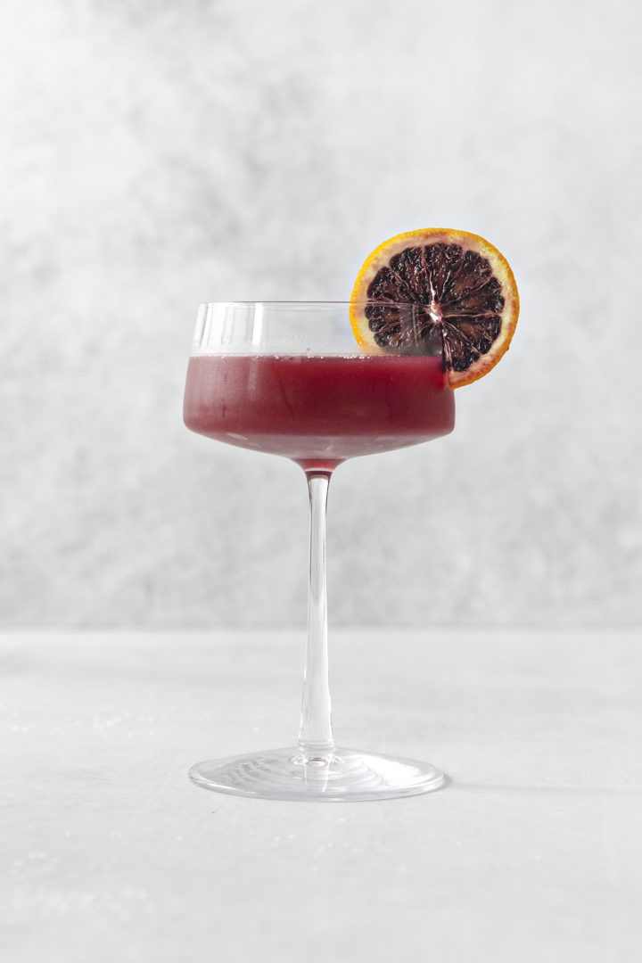 a single glass of blood orange cocktail on a light background