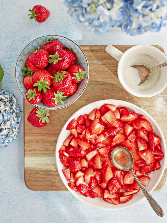 overhead photo of a bowl of macerated strawberries on a cutting board