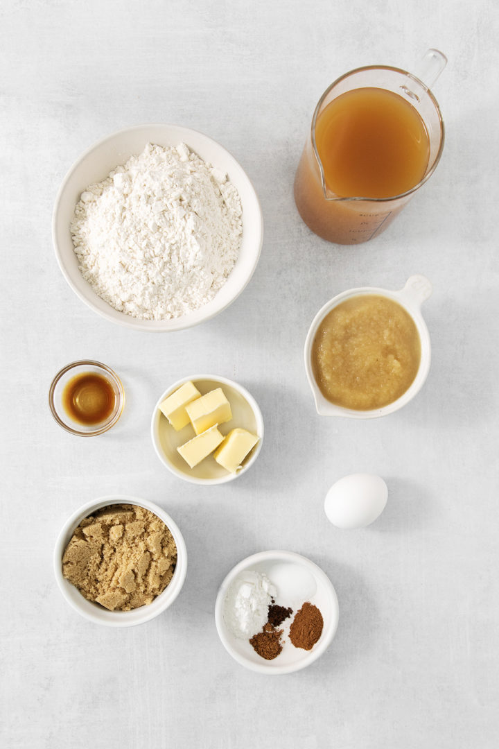 ingredients for apple cider muffins in bowls and measuring cups on a light grey background