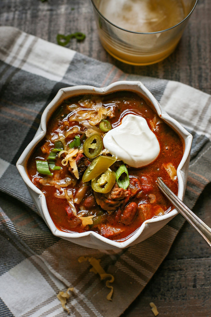 a bowl of brisket chili topped with sour cream, jalapeno, and green onion