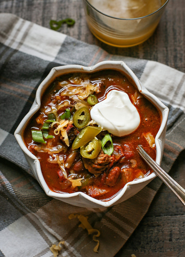 a bowl of brisket chili topped with sour cream, jalapeno, and green onion