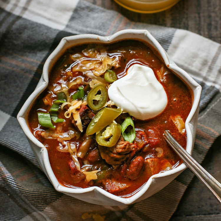 a bowl of brisket chili topped with sour cream, jalapeno, and green onion