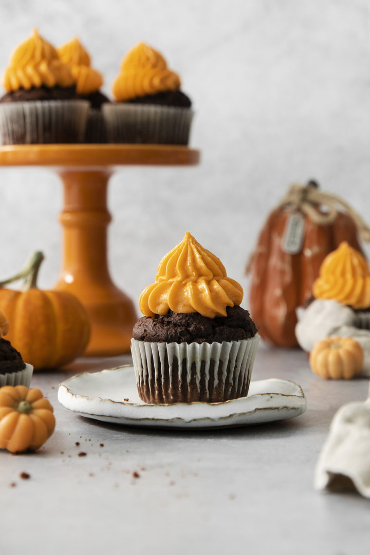 chocolate pumpkin cupcakes for halloween on an orange cake stand surrounded by pumpkins