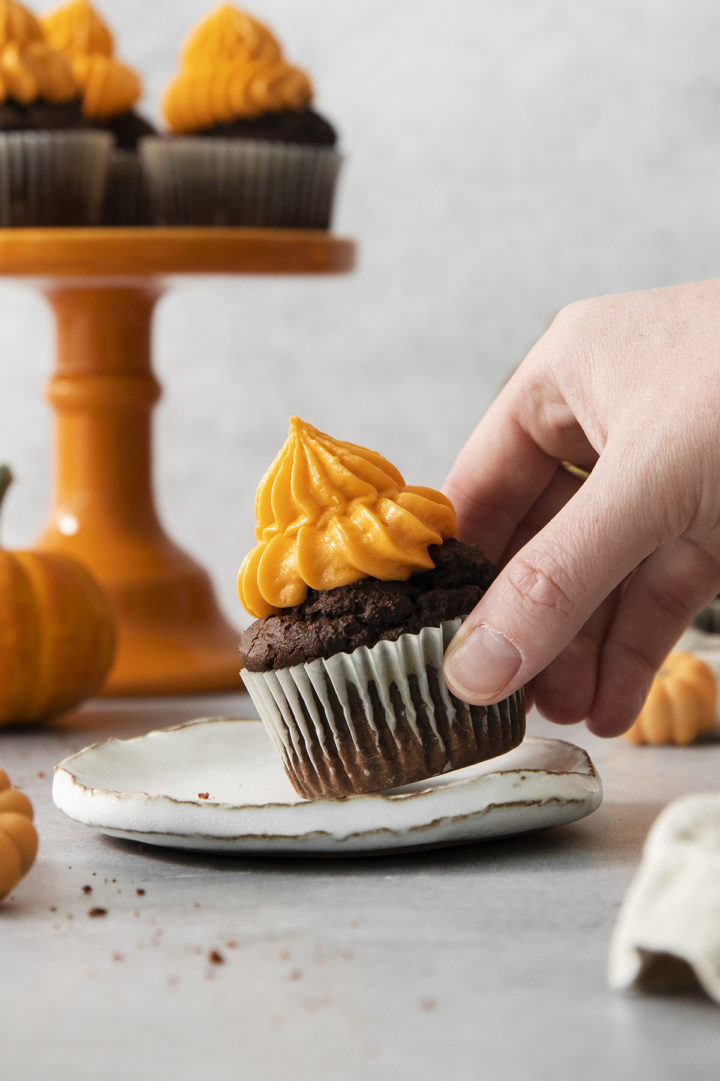 woman picking up a chocolate pumpkin cupcake off of a plate