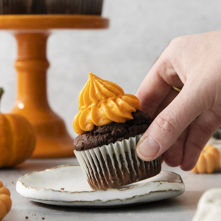 woman picking up a chocolate pumpkin cupcake