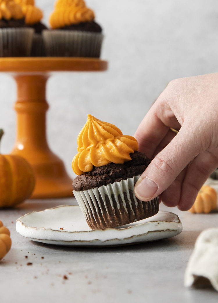 woman picking up a chocolate pumpkin cupcake