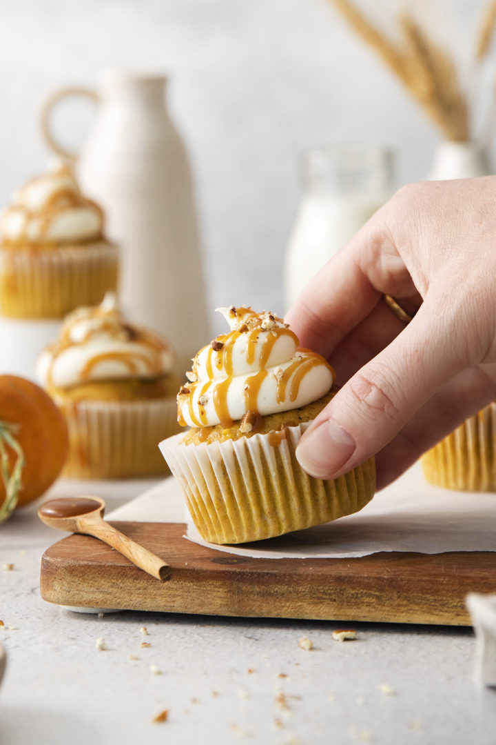 woman picking up a pumpkin cupcake with cream cheese frosting