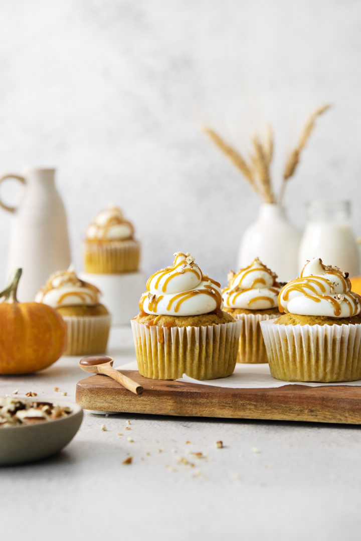 pumpkin cupcakes for fall with fall decor and a wooden cutting board