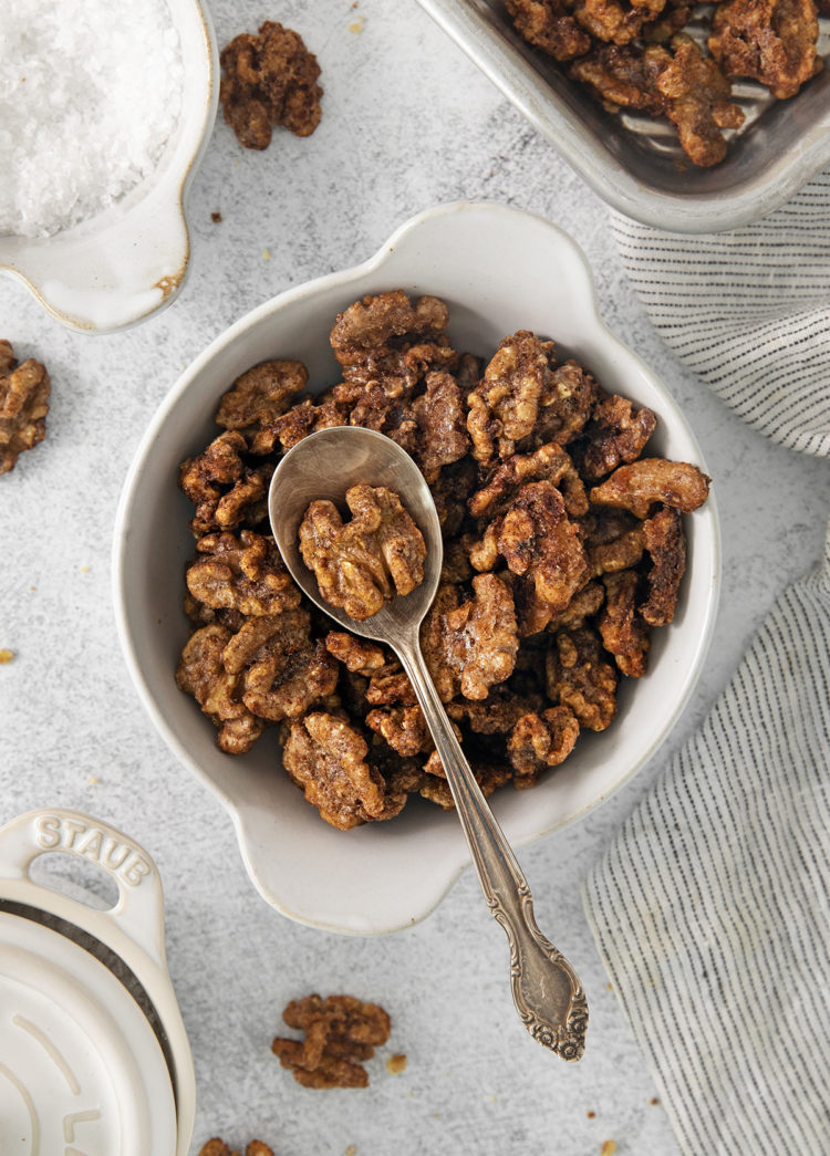 a white bowl full of glazed walnuts with a spoon