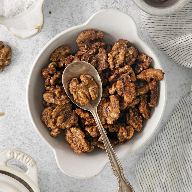 a white bowl full of glazed walnuts with a spoon