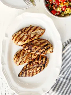 a white platter with cooked grilled chicken breasts that were marinated using balsamic chicken marinade