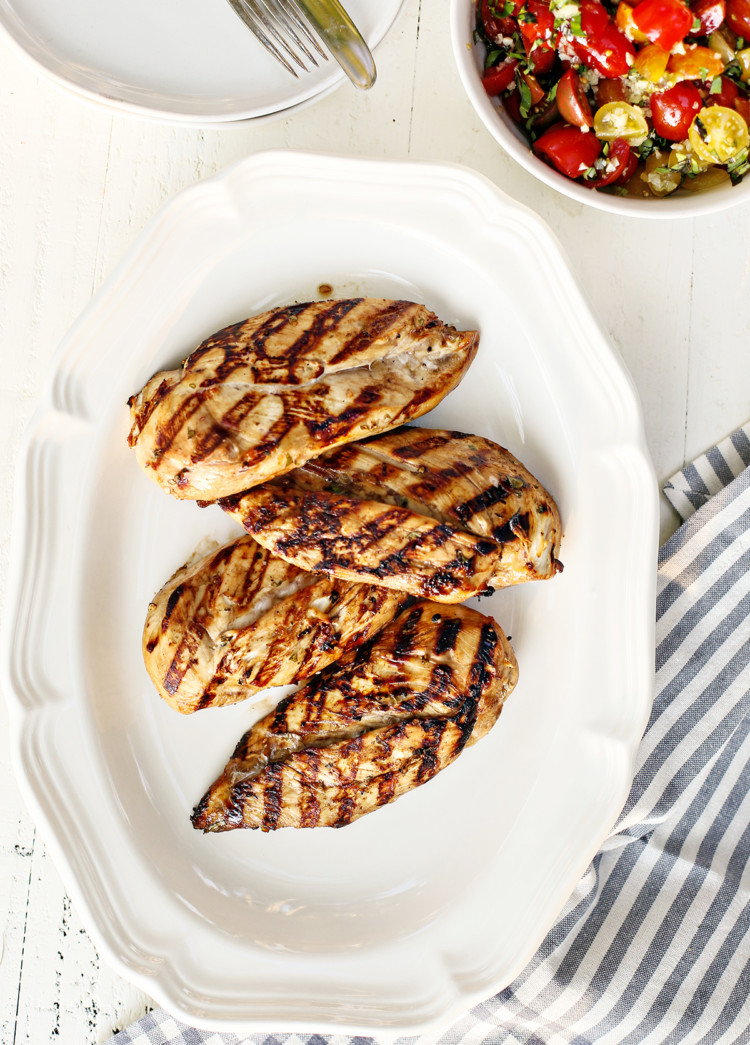 a white platter with cooked grilled chicken breasts that were marinated using balsamic chicken marinade