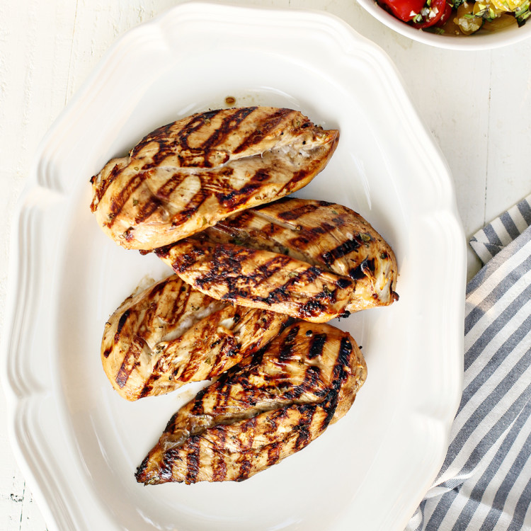 a white platter with cooked grilled chicken breasts that were marinated using balsamic chicken marinade