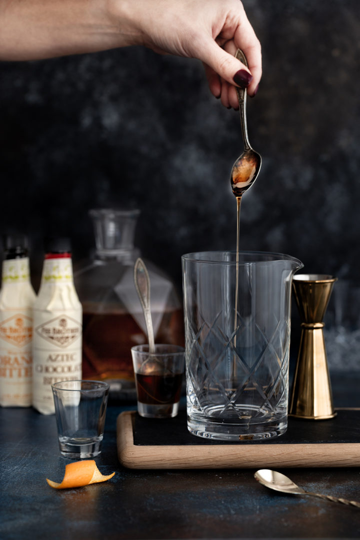 woman adding agave to a cocktail mixing glass while preparing a tequila old fashioned cocktail