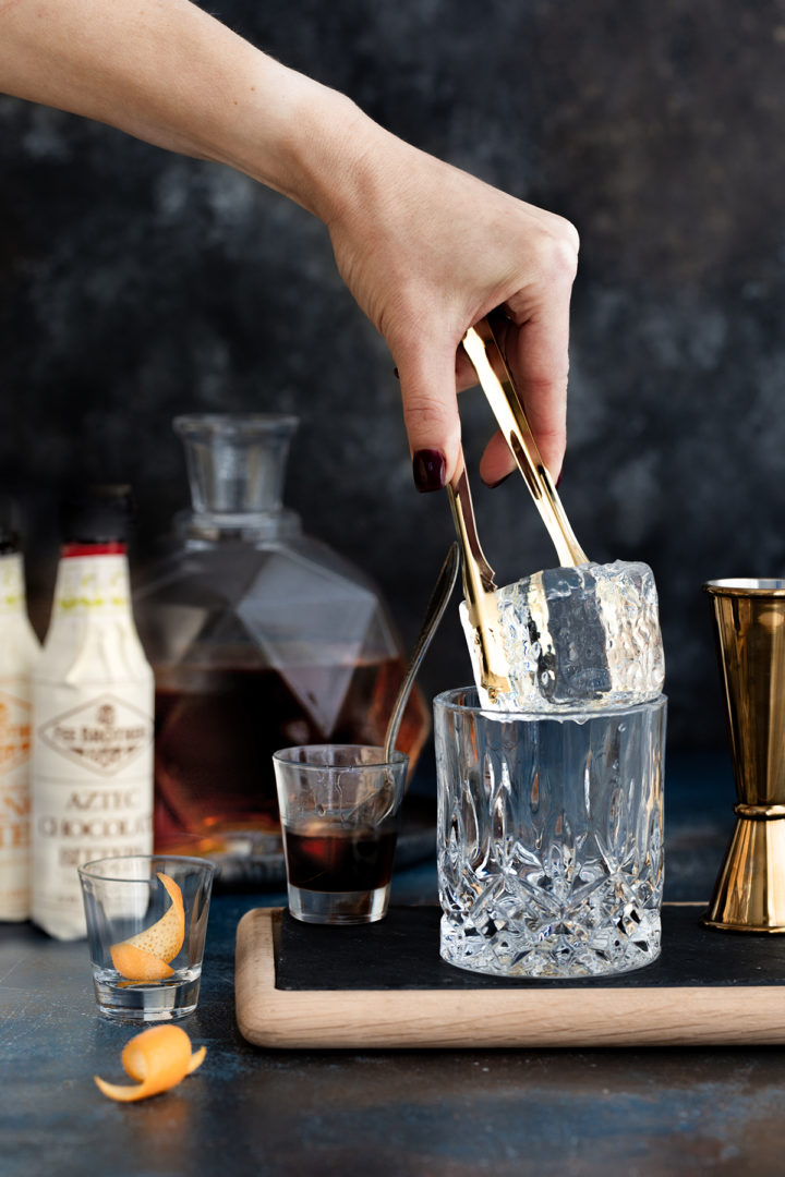 woman adding a clear ice cube to an old fashioned glass