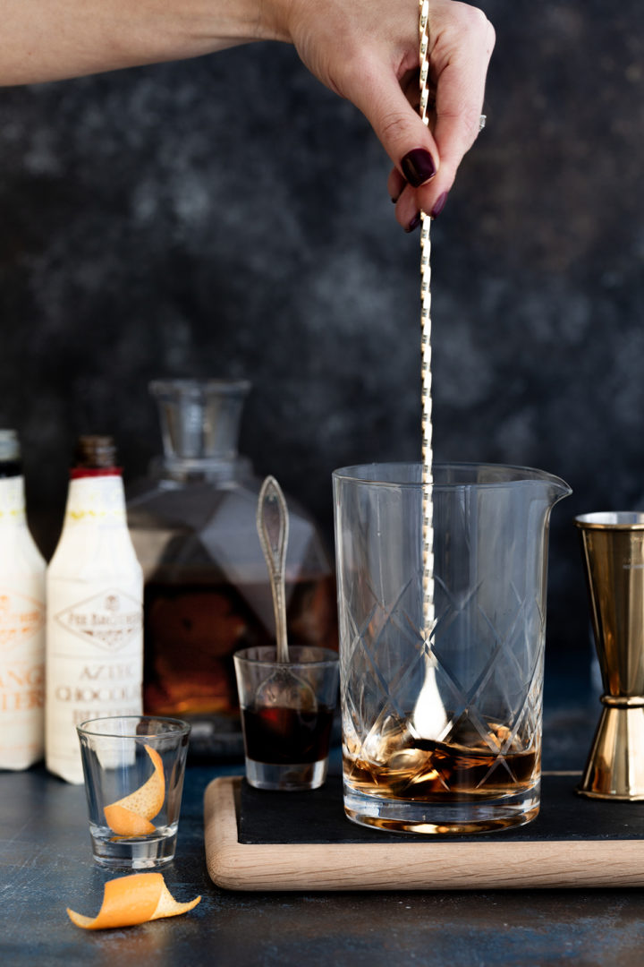 woman stirring ingredients in a tequila old fashioned in a cocktail mixing glass