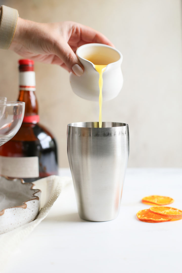 pouring orange juice into a cocktail shaker to make pumpkin martinis