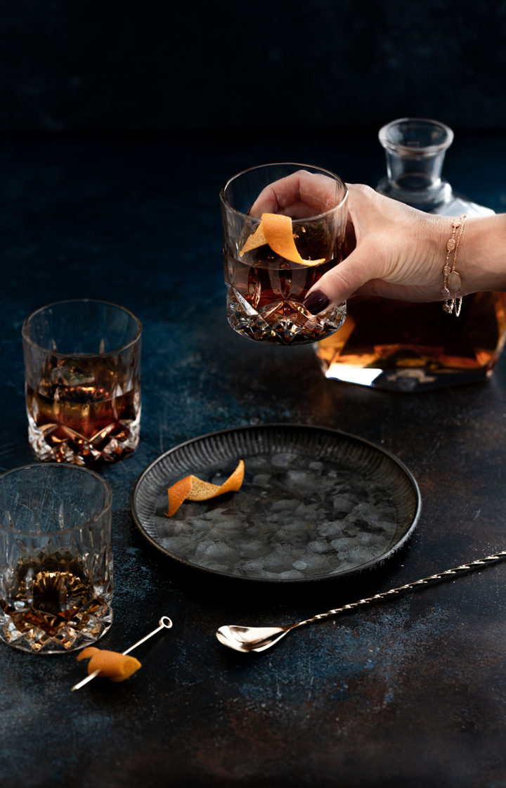 woman picking up a glass with a añejo tequila cocktail