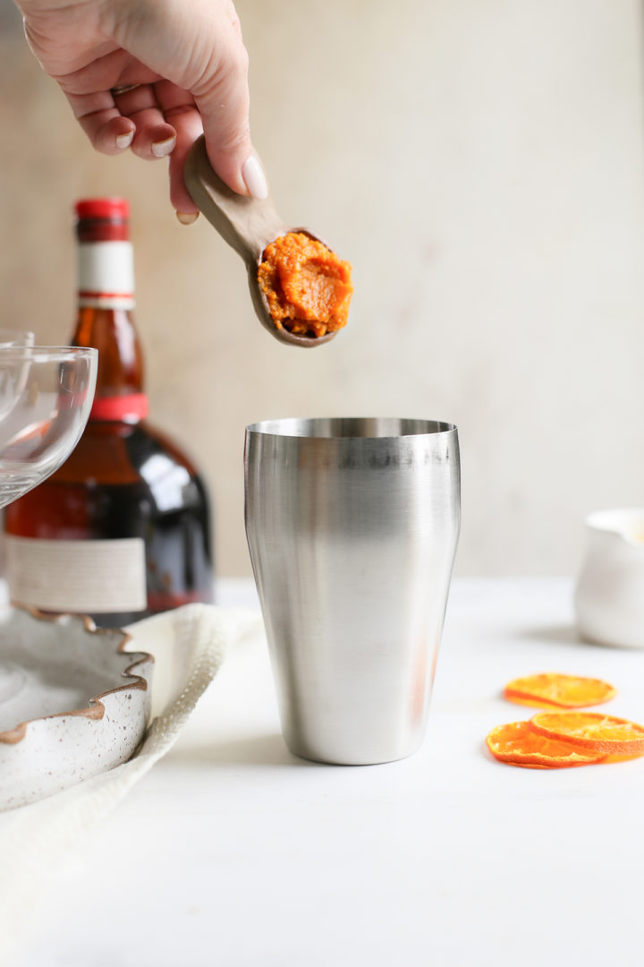 adding pumpkin puree to a cocktail shaker for a fall martini recipe