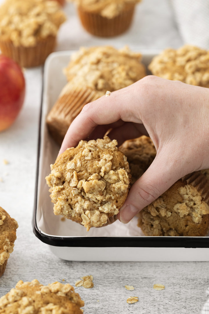 woman picking up an apple crumble muffin