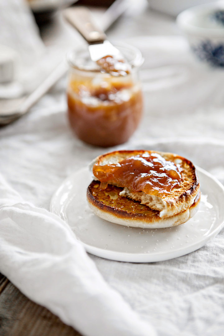 white plate set on a white table cloth with a toasted english muffin spread with homemade pear butter