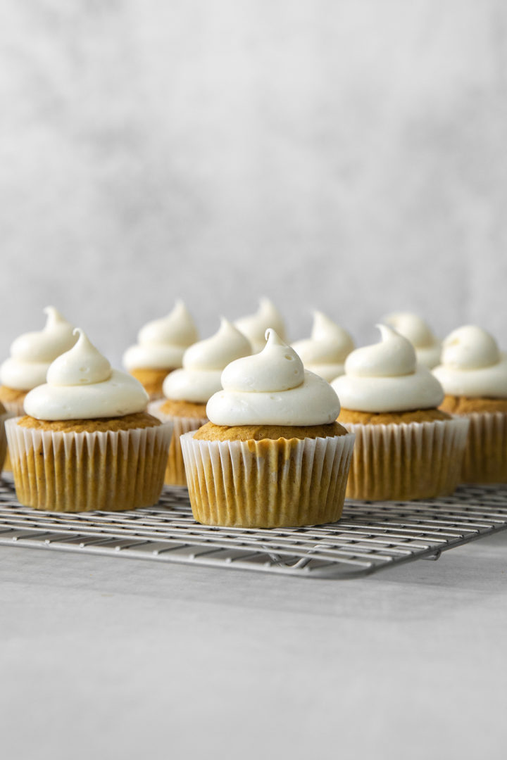 pumpkin cupcakes on a wire rack decorated with cream cheese frosting