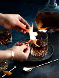 woman making a flamed orange garnish for an old fashioned with tequila
