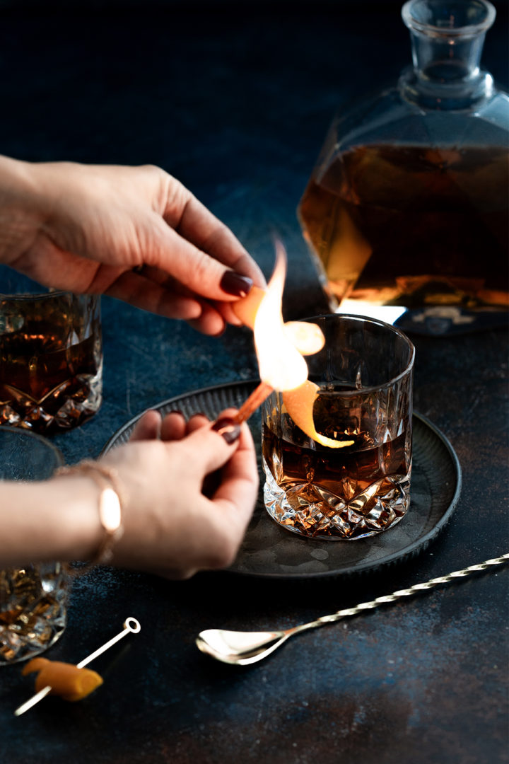 woman making a flamed orange garnish for an old fashioned with tequila