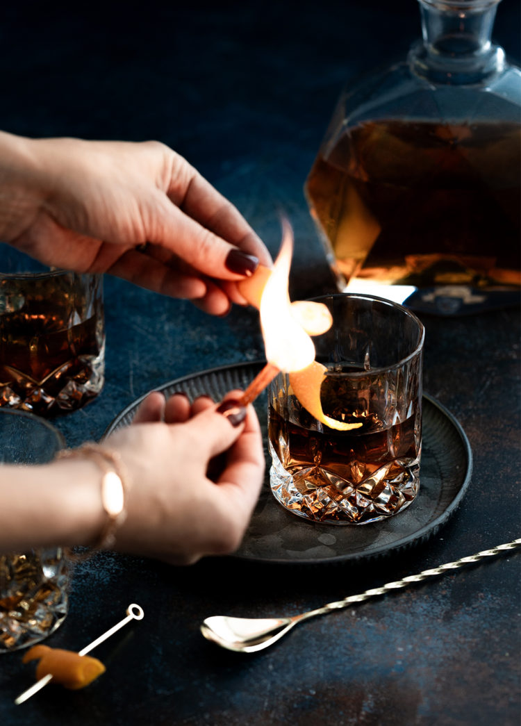 woman making a flamed orange garnish for an old fashioned with tequila