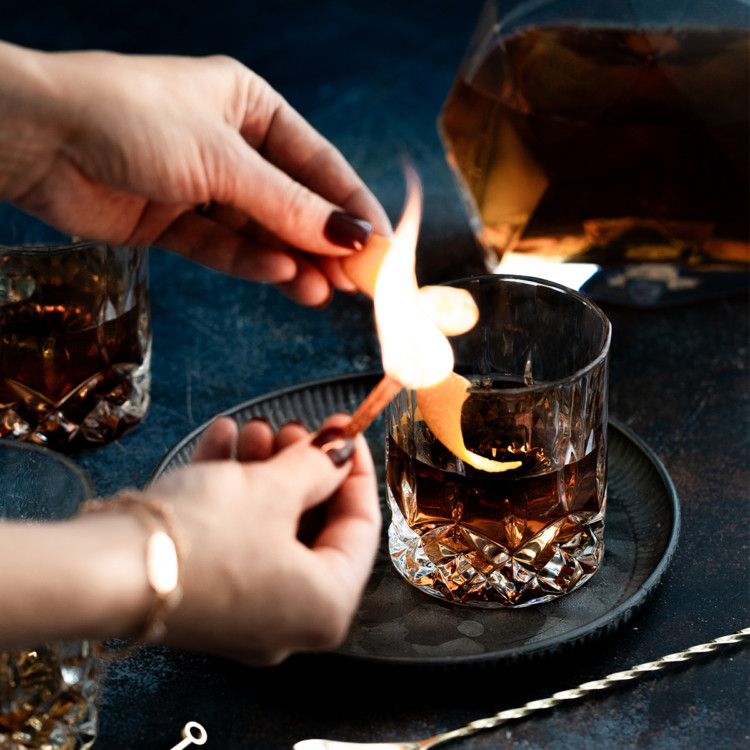 woman making a flamed orange garnish for an old fashioned with tequila