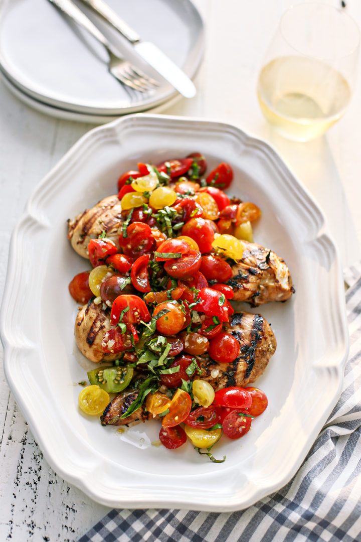 balsamic marinated chicken on a white platter topped with tomatoes and basil
