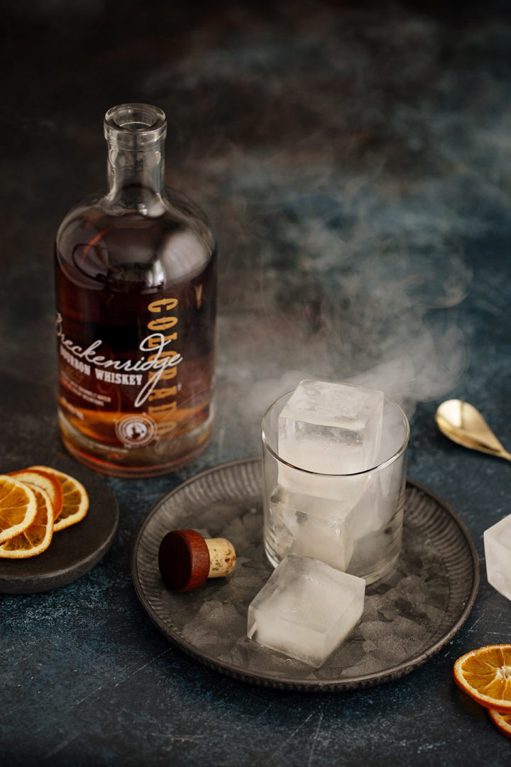 cocktail glass with smoked ice next to a bottle of bourbon whiskey