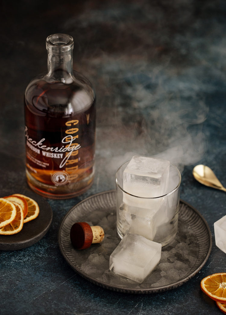 smoked ice in a glass next to a bottle of bourbon