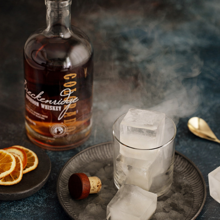 smoked ice in a glass next to a bottle of bourbon