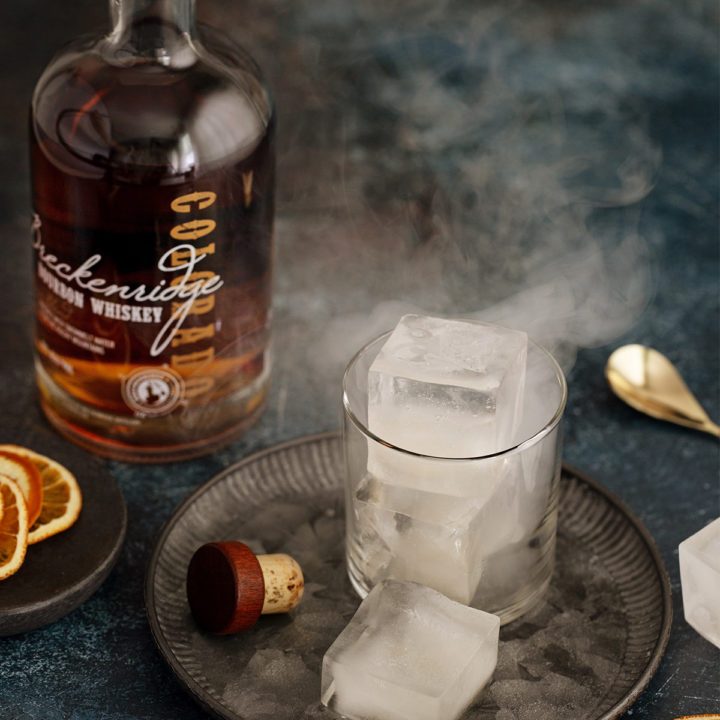 glass of smoked ice cubes next to a bottle of bourbon