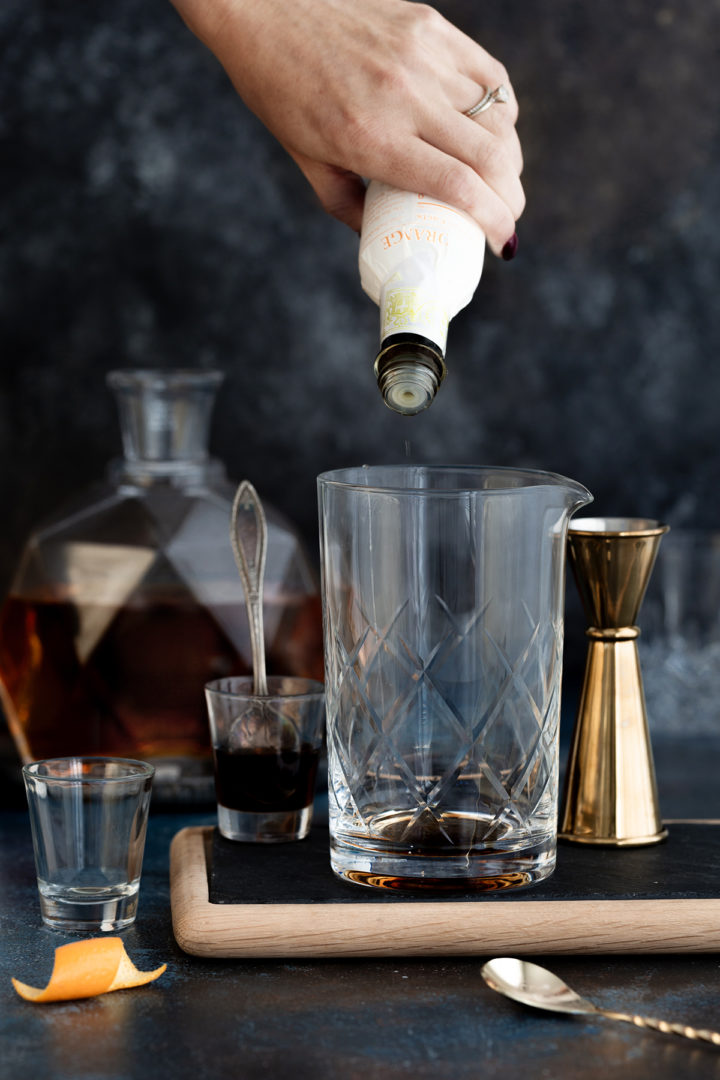 woman adding orange bitters to a cocktail mixing glass as she prepares an añejo tequila old fashioned
