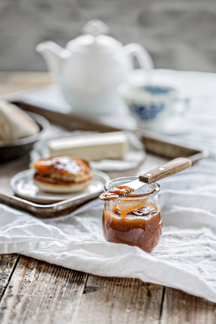 a wooden table set with breakfast, tea pot, tea mug and a jar of canned pear butter