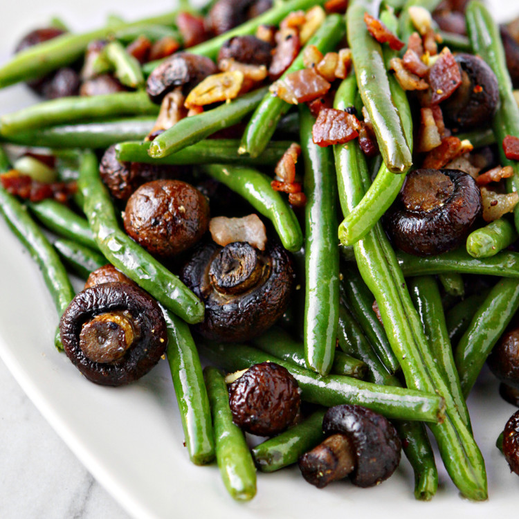 sautéed green beans with mushrooms and bacon on a white platter