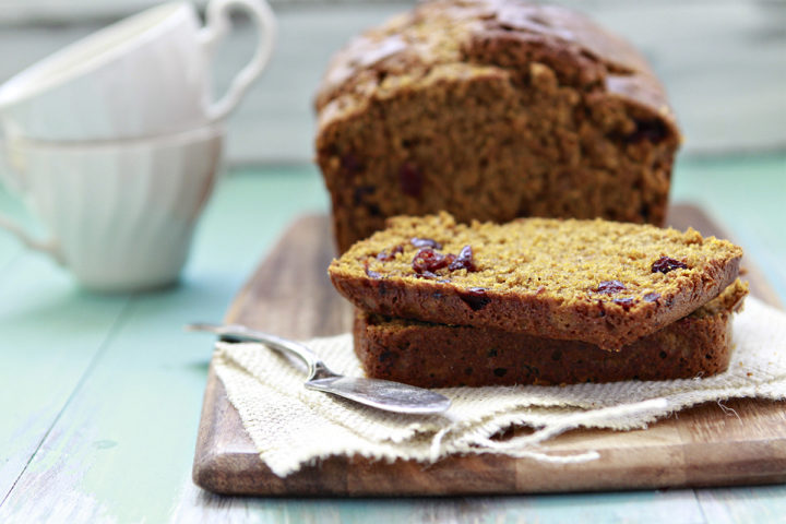 slices of cranberry pumpkin bread on a wooden cutting board with a butter knife