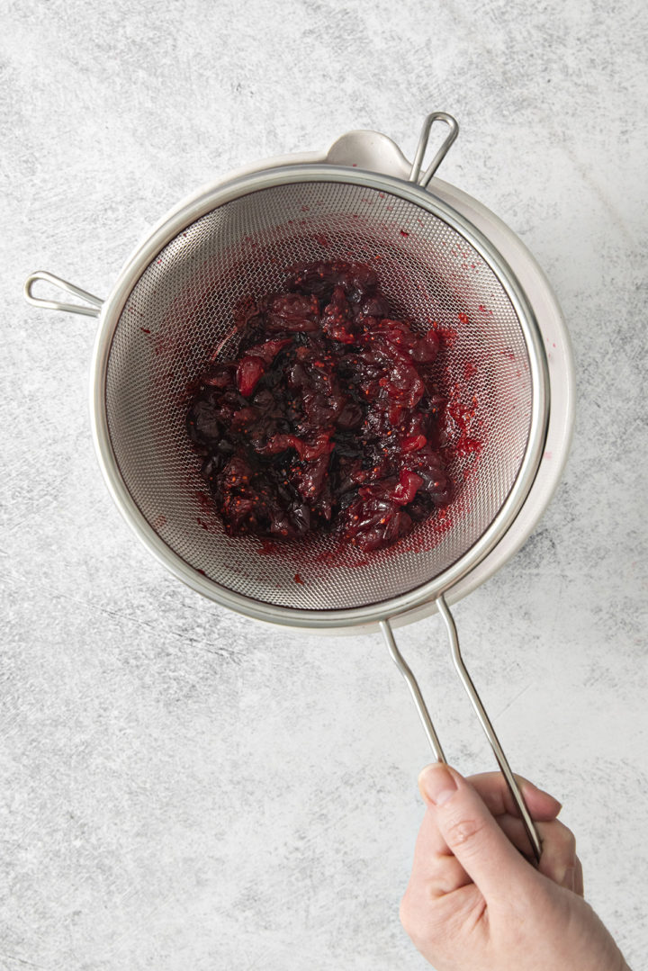 woman straining cooked cranberries after making cranberry simple syrup