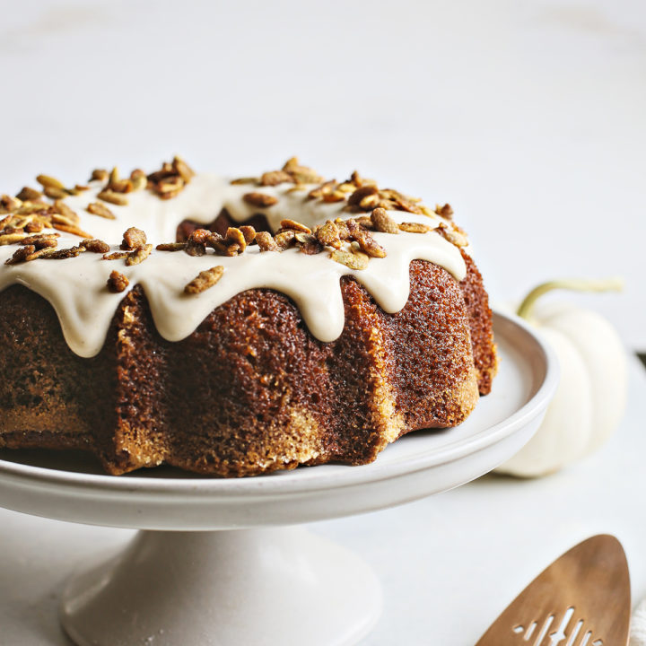 pumpkin bundt cake with cream cheese glaze on a white cake stand