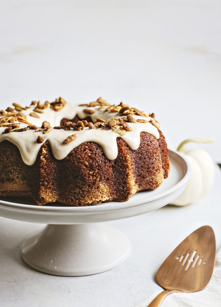 pumpkin bundt cake with cream cheese glaze on a white cake stand