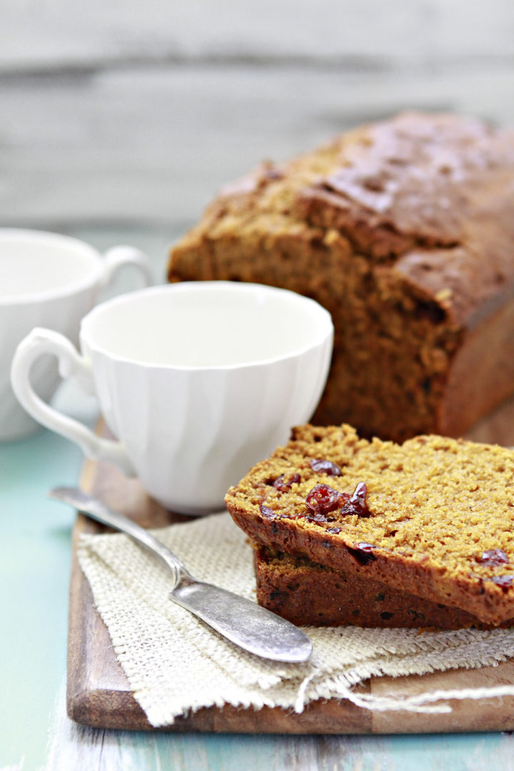 pumpkin cranberry bread sliced on a cutting board with white mugs