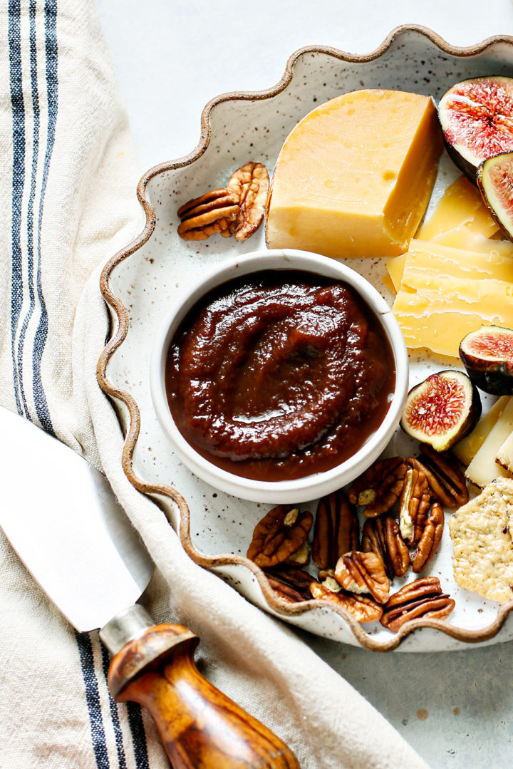 bowl of apple butter on a plate with fruit, nuts, cheese, and crackers