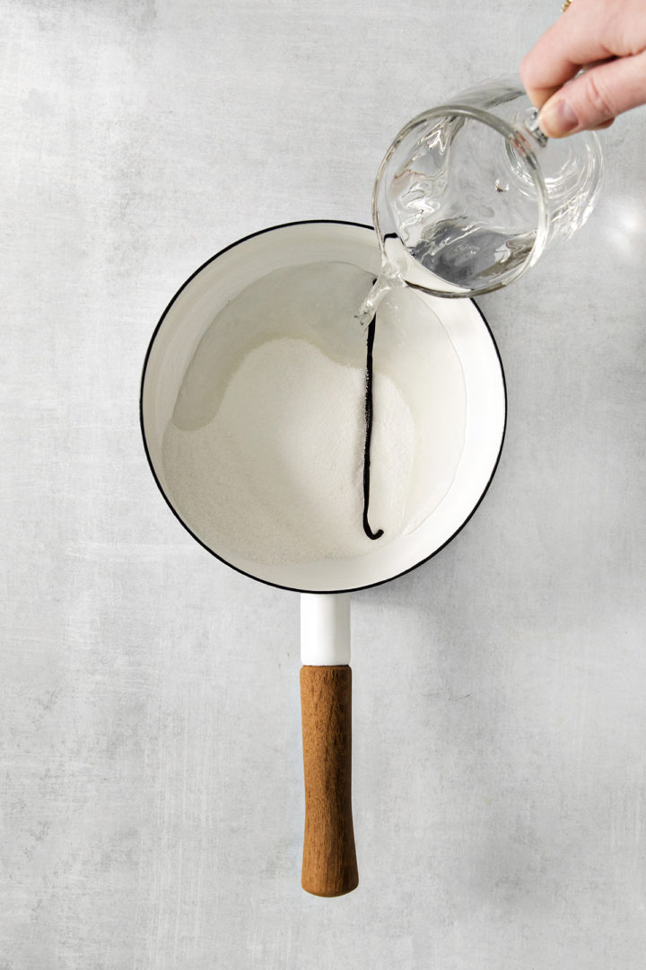 woman pouring water into a pot with vanilla bean and granulated sugar to make vanilla simple syrup