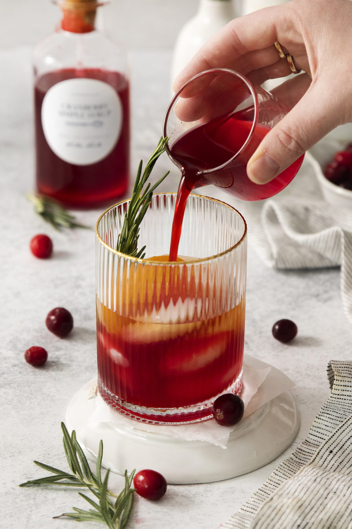 woman pouring cranberry syrup into a cocktail