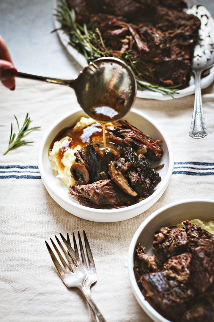 woman pouring graving on a serving of instant pot chuck roast with mashed potatoes