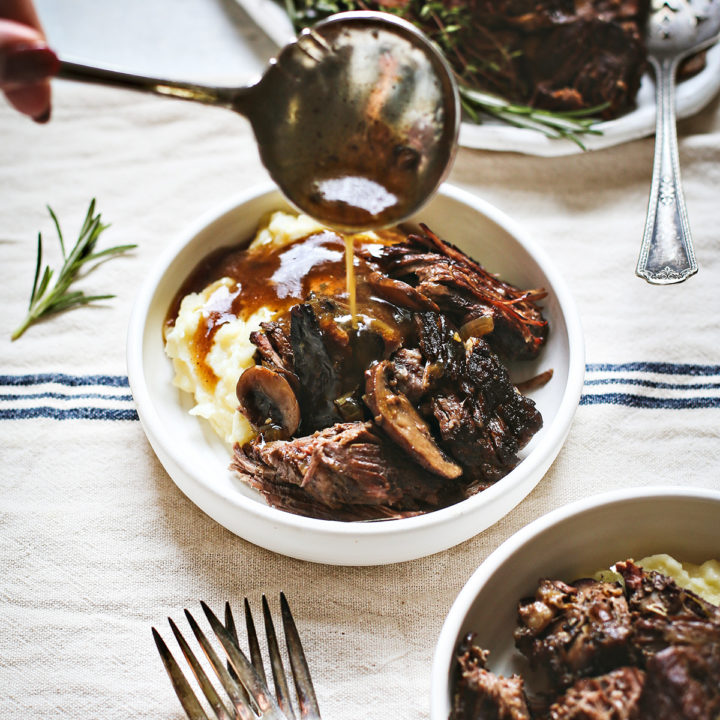 woman spooning mushroom gravy onto a bowl of Instant Pot chuck roast with mashed potatoes