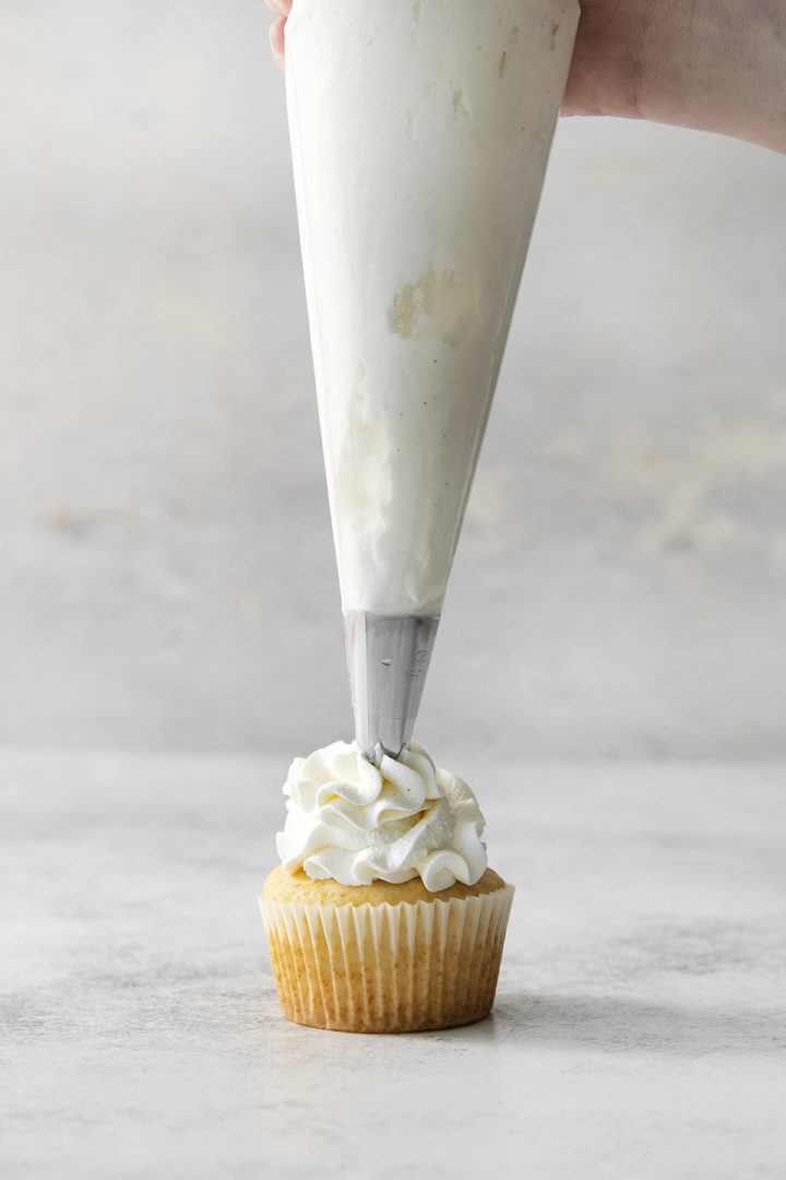 piping stabilized whipped cream with gelatin onto a cupcake