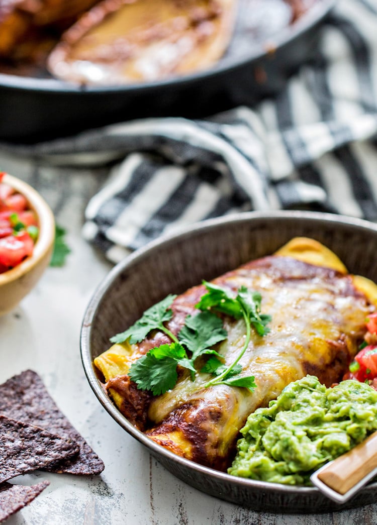 chicken enchiladas on a serving plate with guacamole and pico de gallo